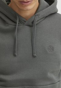 Gray cotton hoodie featuring a front pocket, drawstrings, and a small embossed logo on the chest. Soft texture with a medium thickness.
