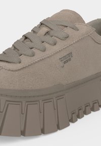 Baskets en daim beige avec semelle épaisse à rainures, lacets gris et logo métallique "tommy jeans" sur le côté.