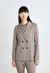 Doppelt breiter Anzugjacke aus einem gemusterten Stoff mit Rautenformen in Beige, Schwarz und Pink. Strukturiertes Design mit schwarzen Knöpfen.