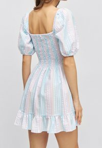 Smocked mini dress with puff sleeves, featuring pastel blue and pink stripes, and a ruffled hemline. Made from lightweight fabric.