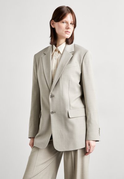 Light grey tailored blazer made of a smooth fabric with two buttons, notched lapels, and a side pocket, paired with a light button-up shirt.