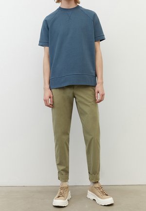 Niebieski, krótko-słodzony sweatshirt o luźnym kroju, z prążkowanym dekoltem i podwiniętymi rękawami, zestawiony z jasnobrązowymi, zwężającymi się spodniami oraz beżowymi trampkami.