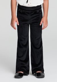 Czarne spodnie typu korduroy z szeroką nogawką, z regulowanym pasem na sznurki i subtelną fakturą prążków, w zestawieniu z czarnymi butami.