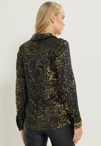 Camicia nera e dorata con paillettes, collo classico, maniche lunghe e vestibilità comoda, caratterizzata da una superficie testurizzata scintillante.