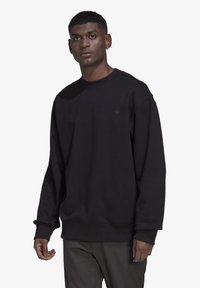 Juodas megztinis, pagamintas iš minkštos medžiagos, su apvalia iškirpte, ilgomis rankovėmis ir susiūtomis rankogaliais. Maža logotipo etiketė ant krūtinės. Laisvas siluetas.