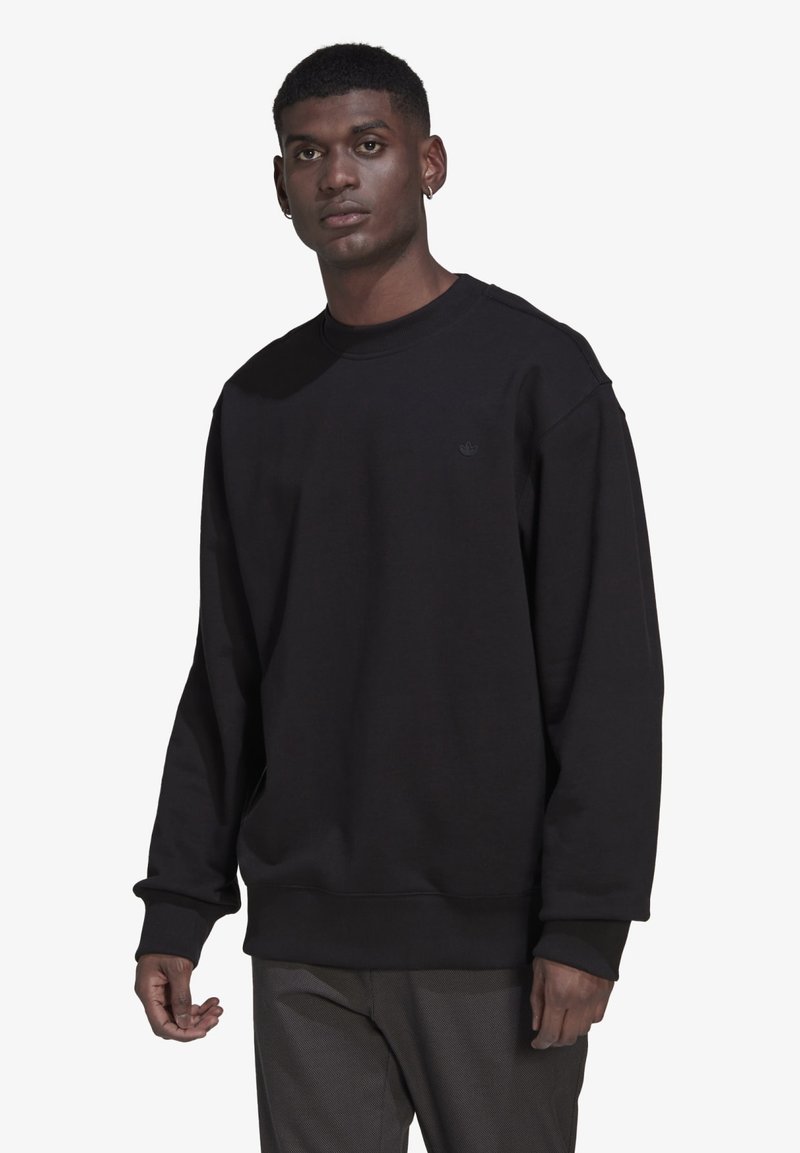 Juodas megztinis, pagamintas iš minkštos medžiagos, su apvalia iškirpte, ilgomis rankovėmis ir susiūtomis rankogaliais. Maža logotipo etiketė ant krūtinės. Laisvas siluetas.