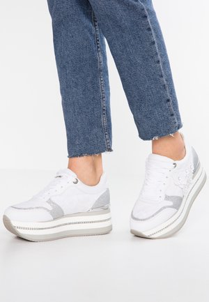 Hvide platform-sneakers med sølvglitterdetaljer, båret med korte blå jeans på en hvid baggrund.