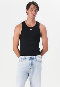 Zwarte tanktop met een ronde halslijn, voorzien van een klein rood logo. Gepaard met lichtblauwe, versleten jeans. Eenvoudig, alsof het goed aansluit.