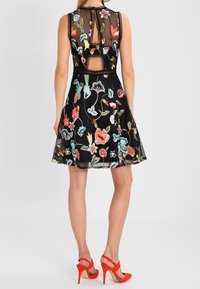 Czarna sukienka z kwiecistym haftem, z przezroczystym tyłem, bez rękawów i rozkloszowanym dołem. Posiada jaskrawe, wielokolorowe wzory kwiatowe.