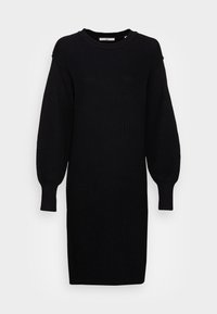 Abito nero in maglia con scollatura tonda, maniche lunghe a palloncino e texture a coste. Silhouette leggermente svasata con taglio a ginocchio.