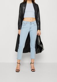 Light blue cropped jeans with a fitted design, paired with a black long coat and black strappy heels, holding a black handbag.