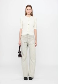 White ribbed short-sleeve cardigan with gold buttons, paired with light denim wide-leg jeans and a small dark handbag. Black shoes.