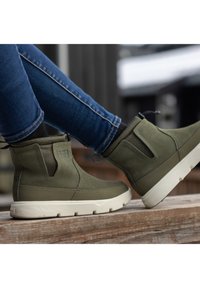 Green suede ankle boots with a white rubber sole, featuring side elastic panels and a pull tab for easy wear.