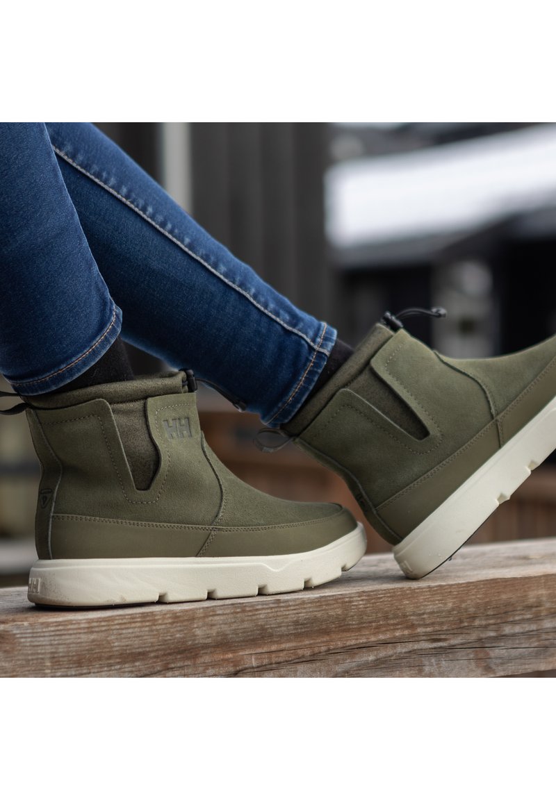 Green suede ankle boots with a white rubber sole, featuring side elastic panels and a pull tab for easy wear.