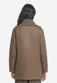 Brun puffjacka med ribbad krage, oversized passform och textil med struktur. Har rakt avslut och långa ärmar.