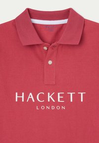 Rotes Polohemd aus strukturiertem Baumwollmaterial, mit einer Knopfleiste mit zwei Knöpfen und dem weißen Logo 'HACKETT LONDON' auf der Brust. Akzentuiert mit einem weißen Kragen.