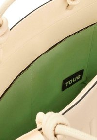 Borsa tote beige con esterno testurizzato, interno verde e chiusura con zip nera. Presenta manici annodati e un'etichetta nera all'interno.