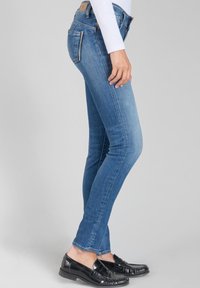 Jean skinny bleu en denim, avec une taille mi-haute, un design à cinq poches et des détails de décoloration subtils. Se marie bien avec des mocassins noirs.