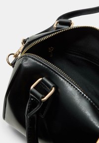 Borsa a tracolla in pelle verniciata nera con zip dorata, vista angolata che mostra i doppi scomparti con zip e la tracolla nera con accenti in oro.