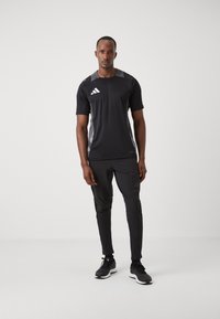 Zwart sportoutfit bestaande uit een shirt met korte mouwen met grijze accenten en bijpassende slim-fit broek, gecombineerd met zwarte sneakers.