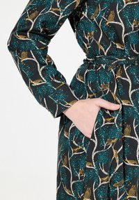 Abito nero con stampa di albero e gufo, presenta maniche lunghe, vita con cintura e tasca laterale. Tessuto testurizzato con colori vivaci.