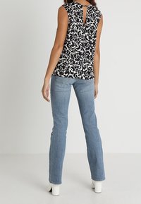 ZWART-WIT PATROON LOZE TOP ZONDER MOUWEN MET EEN KEYHOLE DETAIL OP DE ACHTERKANT, SAMENGEVOEGD MET LICHTBLAUWE FLARE JEANS EN WITTE HAKKEN.