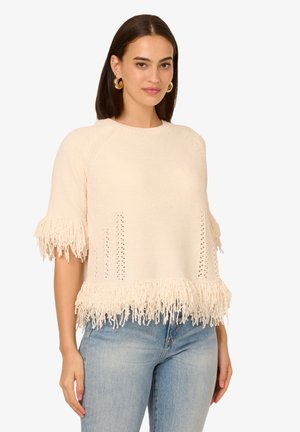 Maglione con frange in crema con lavorazione a maglia texturizzata, dotato di maniche corte, perforazioni laterali e un orlo decorato con lunghe frange.