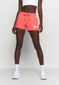 Koralrosa träningstights med dragsko i midjan, med en vit logotyp på vänster ben. Tyget verkar mjukt och lätt.