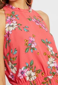 Korálové halter top s květinovým vzorem. Obsahuje volánový výstřih, krátké rukávy a elastický pas. Texturovaná látka s živými barvami.