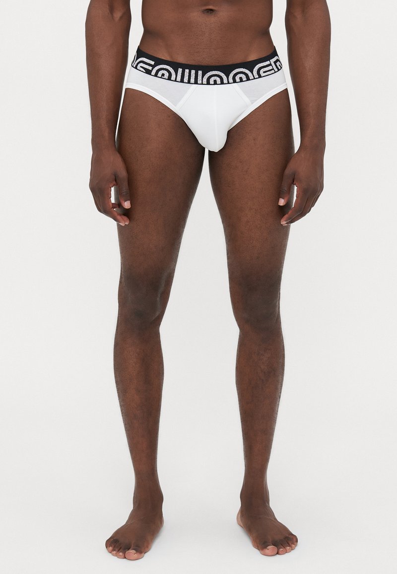 Weißer Slip mit schwarzem elastischem Bund, der ein Logodesign aufweist. Hergestellt aus glattem Stoff, bietet er eine enge Passform und minimale Bedeckung.