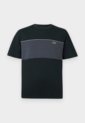 Camiseta de algodón negra con un panel horizontal en gris oscuro que contrasta y detalles de costura blanca; acento de logo verde en el pecho.