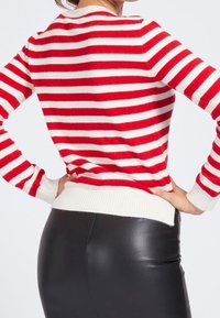 Punavalkoraidallinen pusero, jonka pääntiessä ja helmassa on resori, pitkähihaisen ja pehmeän tekstuurin omaava, puettu mustien housujen päälle.