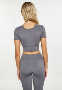 Szürke, rövid ujjú, cropped sporttop, varrás nélküli kialakítással és varrási részletekkel, párosítva hozzá illő, szürke, magas derekú leggingssel.