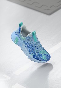 Mėlyna Nike kedų pora su mozaikos raštu, kuriame derinami įvairūs mėlyni ir žali atspalviai, šviesiai mėlynas padas ir tekstūruota viršutinė medžiaga.