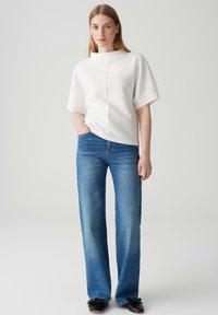 Top bianco texturizzato con maniche corte, caratterizzato da una cucitura unica. Abbinato a jeans in denim blu a gamba dritta e scarpe basse nere.