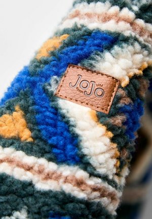 Wełniany materiał z niebieskimi, zielonymi, pomarańczowymi i białymi wzorami. Zawiera brązową skórzaną naszywkę z logo "JoJo". Gruba, teksturowana powierzchnia.