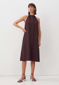 Bordeauxfarbiges Neckholderkleid mit entspannter Passform, knie-lang, mit gefaltetem Hals und glatter Textur, kombiniert mit schlanken schwarzen High-Heels.