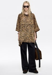 Camisa de estampado de leopardo con un corte holgado, mangas cortas y un cuello con cordón ajustable. Combinada con jeans negros de pierna ancha y un bolso marrón.