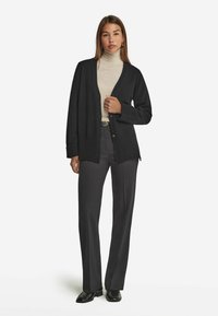 Czarny kardigan z prążkowanymi mankietami i dołem, noszony na jasnej golfie. Zestawiony z ciemnymi spodniami o wysokim stanie i czarnymi butami.