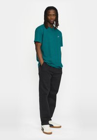 Teal t-shirt met korte mouwen en een ronde hals, gecombineerd met zwarte broek en witte sneakers met marineblauwe accenten. Eenvoudig ontwerp, geen patronen.