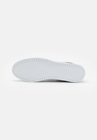White sneaker sole with textured surface, featuring a ribbed pattern along the edges. Material appears rubbery and flexible.
