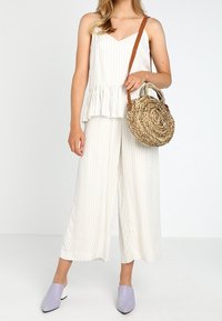 Top peplum bianco a righe, pantaloni palazzo, mule lavanda e una borsa rotonda intrecciata con una tracolla marrone. Tessuto testurizzato e colori morbidi.