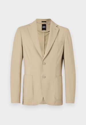 Beige Blazer aus strukturiertem Stoff. Verfügt über einen Reverskragen, zwei Knöpfe, eine Brusttasche und zwei aufgesetzte Taschen vorne.