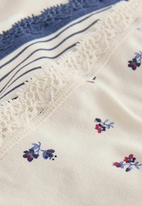 Gros plan de trois morceaux de tissu pliés avec des bordures en dentelle ; un avec un petit imprimé floral, un rayé et un en dentelle bleue unie.