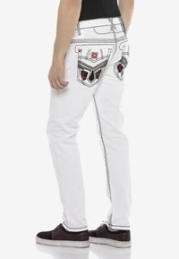 Weiße Jeans aus Denim mit schwarer Naht und dekorativ bestickten Taschen mit roten Akzenten. Figurumspielender Schnitt mit schmal zulaufendem Bein.