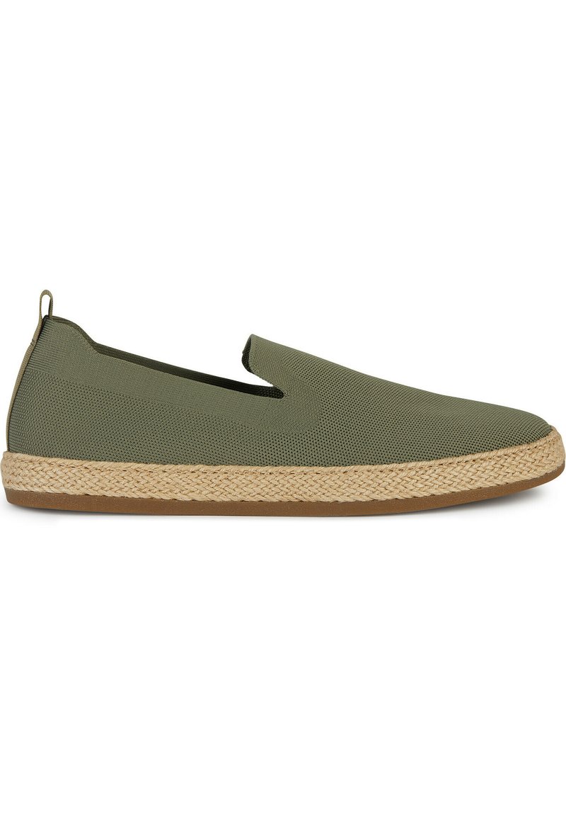 Zapato verde de tipo slip-on con parte superior texturizada, media suela de yute trenzado y suela de goma. Presenta un diseño minimalista y aberturas laterales elásticas.