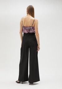 Rimpelige tanktop in roze en zwart dierenprint, gecombineerd met hoge, wijde zwarte broek en zwarte hakken.