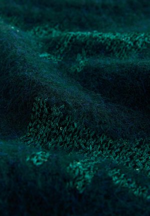 Grüner Textilstoff mit einer weichen, flauschigen Oberfläche; zeichnet sich durch unterschiedliche Farbtöne und ein Strickmuster aus, das Schlaufen und Nähte zeigt.