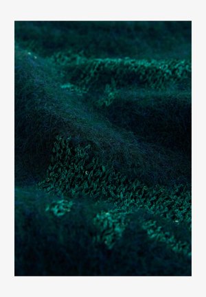 Zaļš teksturēts audums ar mīkstu, pūkainu virsmu; tam ir dažādas nokrāsas un adījuma raksts, kas izceļ cilpas un šuves.