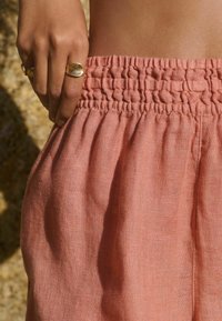 Perzikkleurige linnen broek met een smock-elastische tailleband. De stof heeft een zachte, gestructureerde afwerking met een delicate val.